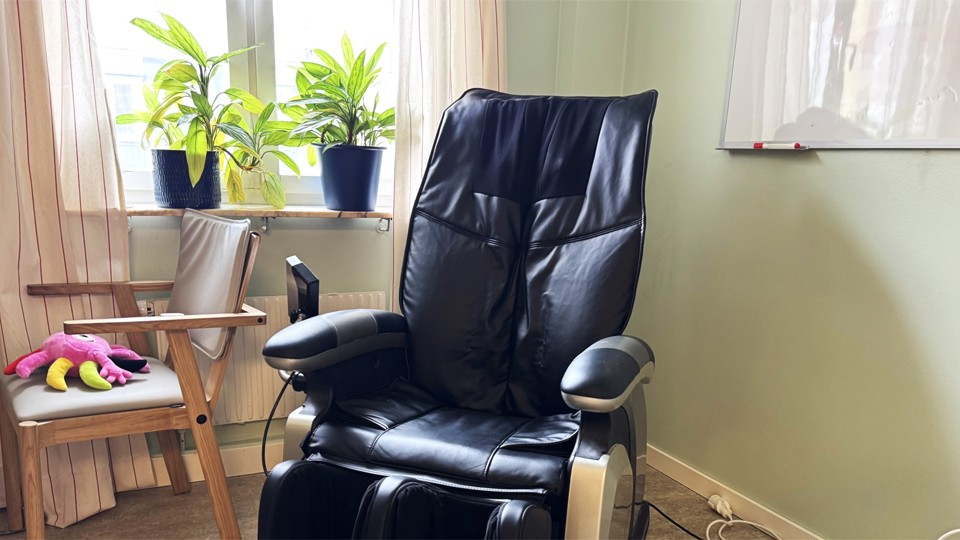 En svart massagestol står invid ett fönster med krukväxter.