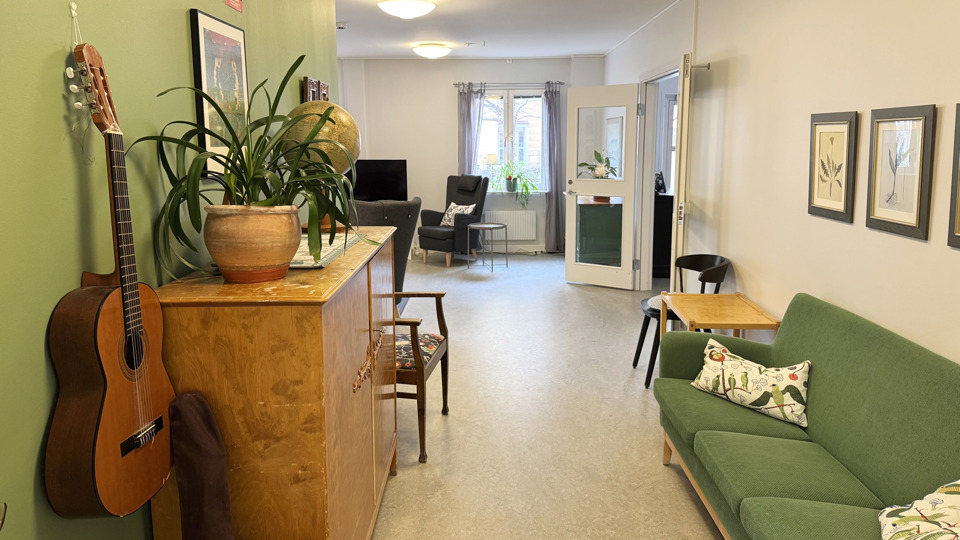 Korridor med grön soffa mot väggen och en gitarr på väggen. Leder till ett allrum.