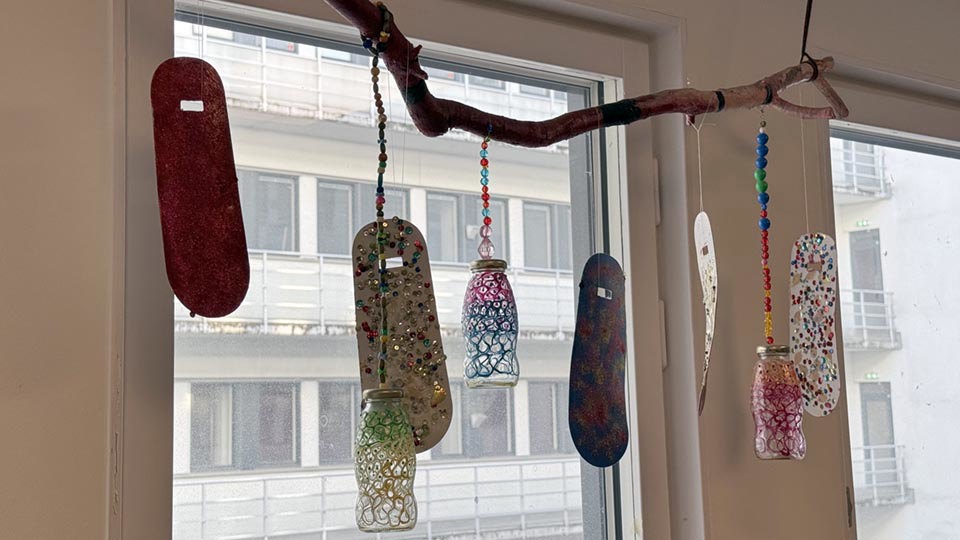 Trädgren i ett fönster med dekorationer som hänger i papper och glas.
