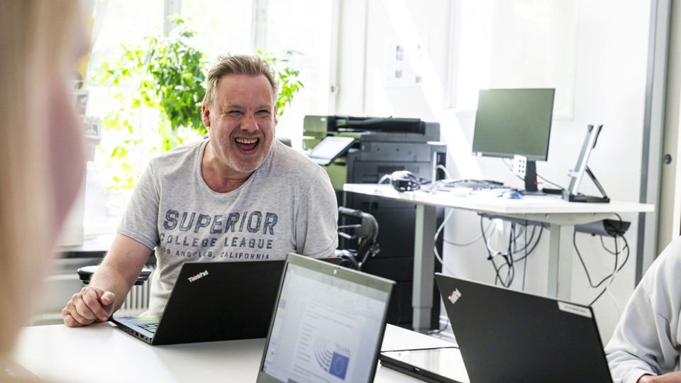En man sitter vid sin dator och ser mycket glad ut.