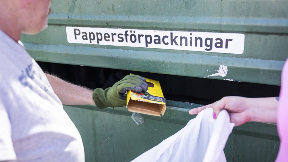 En man står vid en återvinning för papper och kastar skräp.