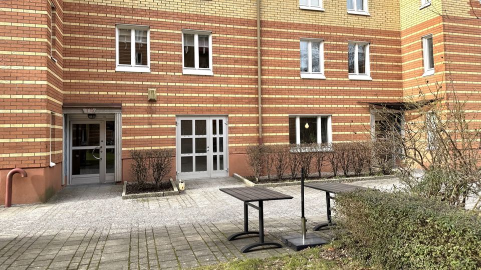 En tegelbyggnad i flera våningar. Framför entrén finns en uteplats.
