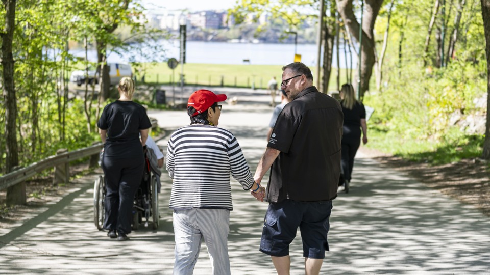 Människor på promenad i omgivningen. Man ser Mälaren, träd och buskar.