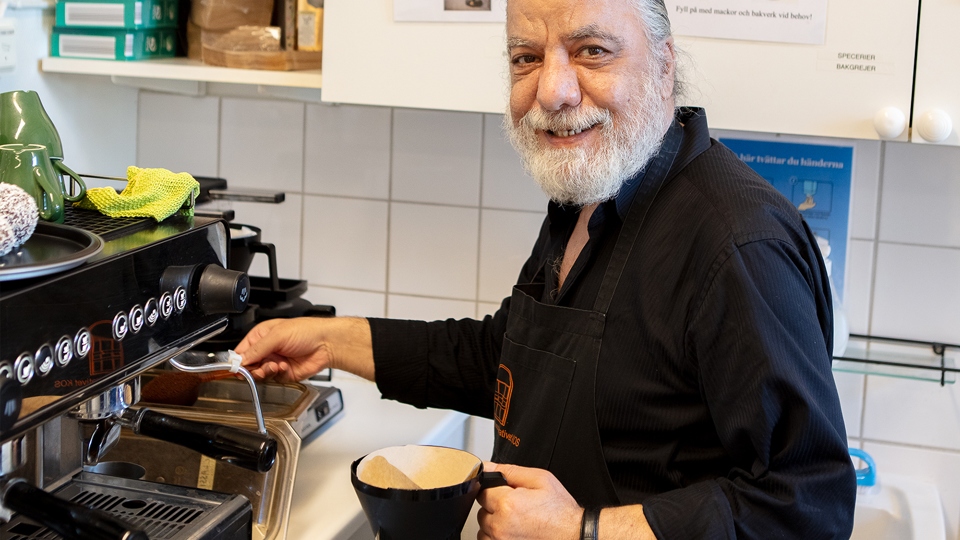 En man håller på med att fylla på kaffe i en kaffemaskin.