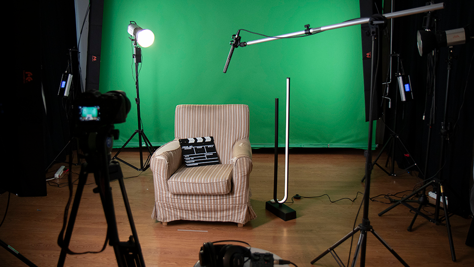 En filmstudio med kameror och mikrofoner riktade mot en fåtölj framför en grön skärm.