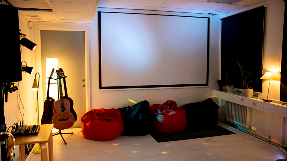 Ett rum med en stor filmduk, gitarrer och saccosäckar. 