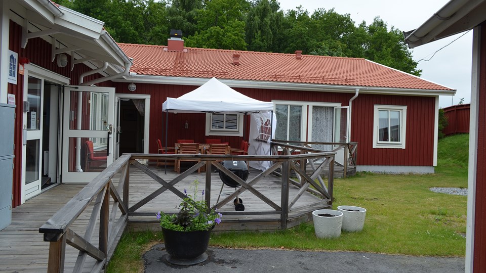 Svanholmens röda träbyggnad och gemensamma altan med utemöbler och parasoll.