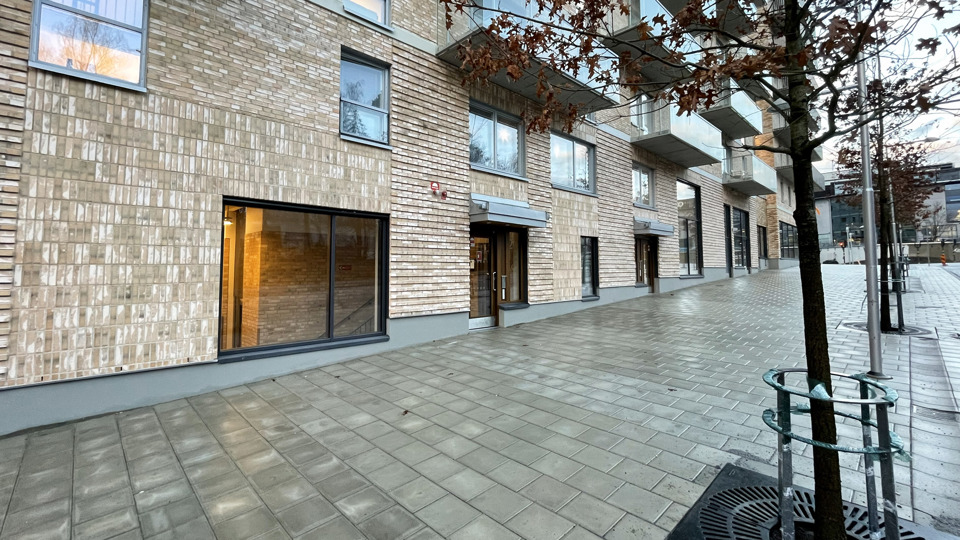 Fasaden på en modern byggnad med stora fönster och ett träd på gångvägen.