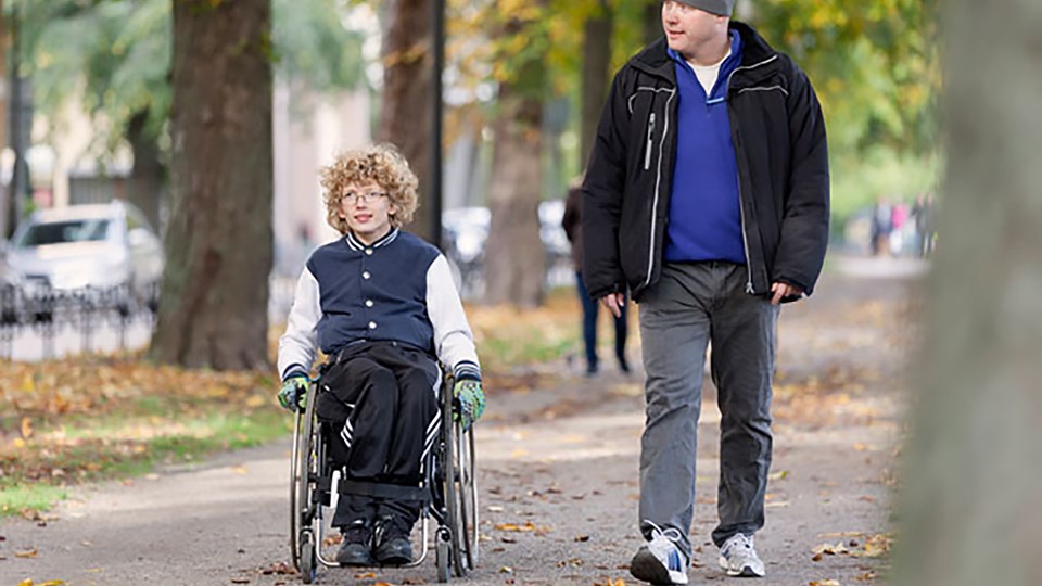 En man går bredvid en pojke som sitter i rullstol.